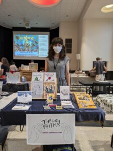 Photo of Theora standing behind her table at Autoptic, wearing a mask.